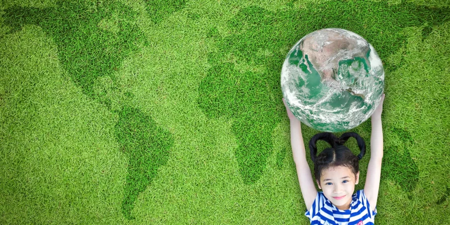 Immagine che mostra una bambina che tiene in mano il pianeta Terra, con lo sfondo di un prato verde che disegna una mappa del mondo. L'immagine rappresenta il concetto di ridurre l'impatto ambientale e l'importanza di prendersi cura del nostro pianeta per le generazioni future.