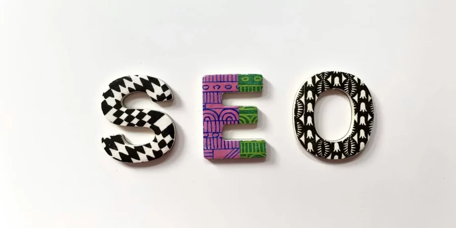 Lettere colorate "S", "E" e "O" decorate con motivi geometrici in bianco e nero e altre combinazioni di colori, disposte per formare la parola "SEO" su uno sfondo bianco