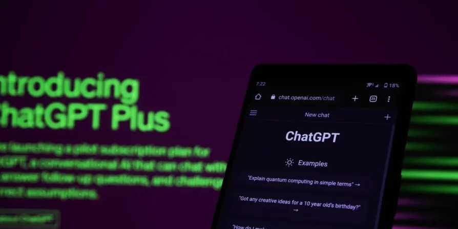 Un primo piano di uno smartphone che mostra l'interfaccia di ChatGPT con la scritta "Introducing ChatGPT Plus" in verde brillante sullo sfondo. La schermata include un esempio di domanda, "Explain quantum computing in simple terms?" e il logo di ChatGPT