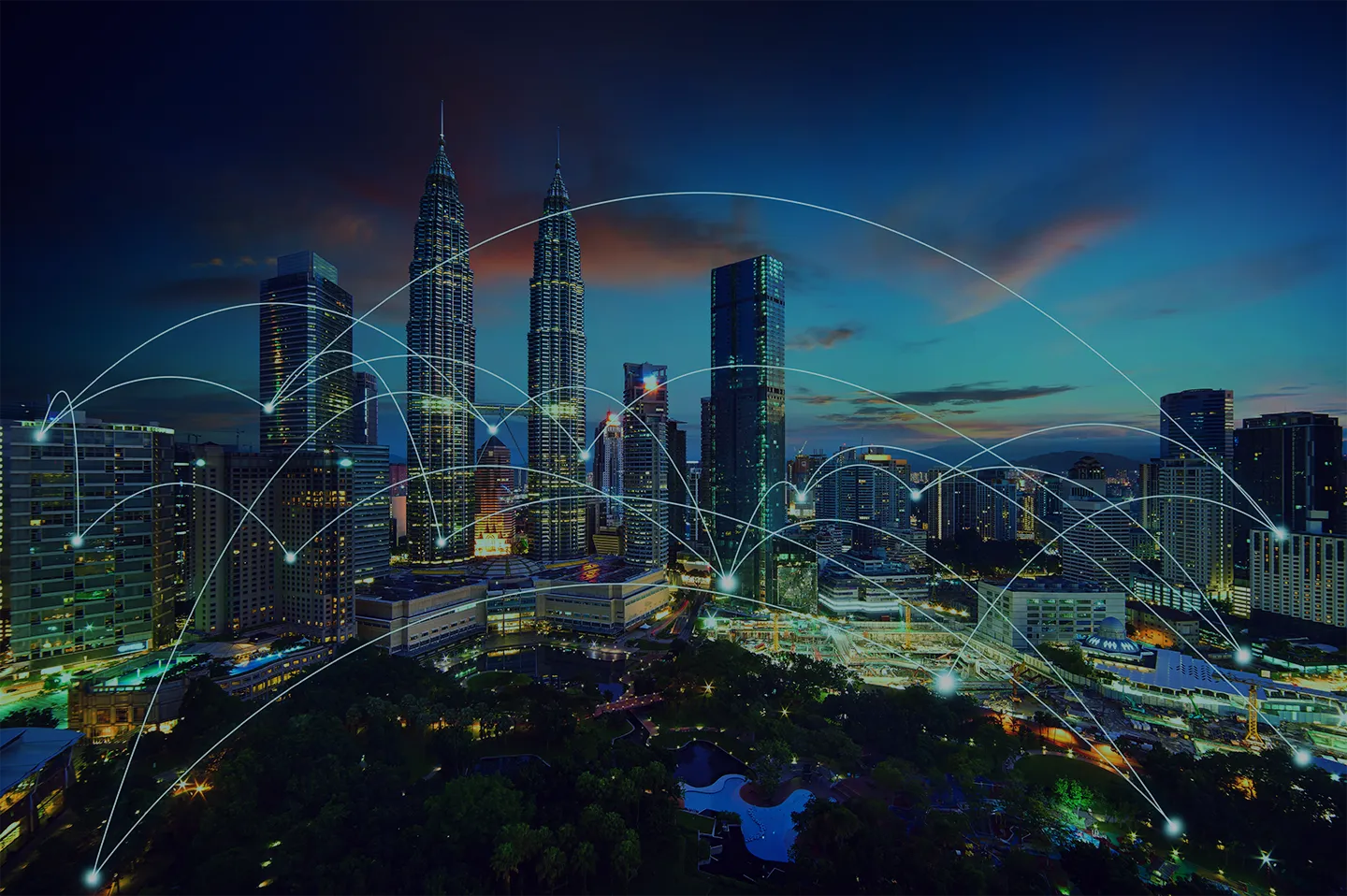 L'immagine mostra uno skyline urbano notturno con grattacieli illuminati. Le linee luminose si intrecciano sopra la città, rappresentando le connessioni della rete dell'Internet of Things (IoT) che collegano vari dispositivi e infrastrutture in una smart city.